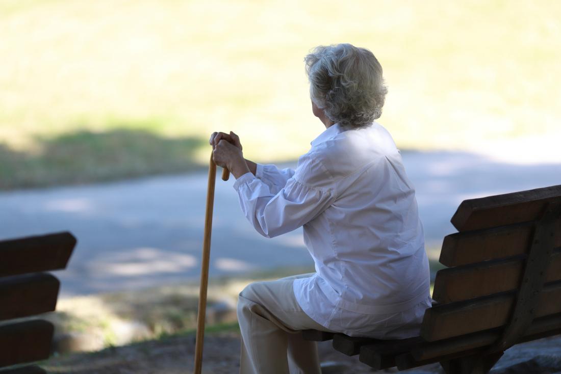 older woman with her back turned to the camera leaning on a cane
